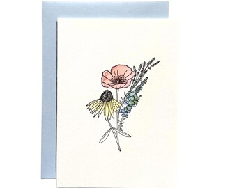 Puede incluir: Una tarjeta de felicitación blanca con una delicada ilustración en acuarela de un ramo de flores que incluye una amapola rosa, una equinácea amarilla y ramas de lavanda azul, acompañada de un sobre azul claro colocado detrás de la tarjeta.