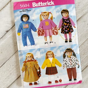 May include: A vintage Butterick sewing pattern, number 5604, for doll clothing. The pattern shows illustrations of dolls in different outfits, such as a blue tracksuit, cheerleader outfit, and a polka-dot dress. The pattern is marked "ONE SIZE".