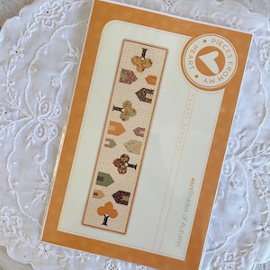 Peut inclure: Un paquet de projet artisanal sur le thème de l'automne. Le motif comprend des maisons et des arbres stylisés aux couleurs automnales. Le texte sur l'emballage indique "#823 Shades of Autumn" et "Pieces From My Heart".