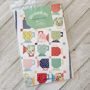 Puede incluir: Un patrón de acolchado para un camino de mesa llamado "Good Morning Mug" de Lori Holt de Bee in My Bonnet. El patrón presenta un fondo blanco con tazas coloridas en un patrón repetitivo.