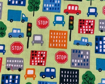 May include: A green fabric with a repeating pattern of red, blue, and yellow cars, buildings, trees, and stop signs. The pattern is on a light green background.