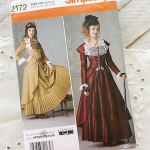 May include: A Simplicity sewing pattern envelope 2172, size HH 6, 8, 10, 12, featuring illustrations of two long-sleeved dresses with ruffled collars, fitted bodices, and pleated skirts. One dress is mustard yellow, and the other is deep red.
