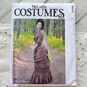 May include: A McCall's Costumes sewing pattern envelope, model M8191, featuring a brown dress with a ruffled skirt and a bright green accent. The text includes 'McCall's COSTUMES', 'M8191', 'SIZE A5 (6-8-10-12-14)', and 'Angela Clayton' on the front.
