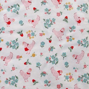 Op de afbeelding: Witte stof met een herhaald patroon van roze kippen met rode schorten en sjaals, afgewisseld met blauwe, gele en roze bloemstukken en rode aardbeien. Een charmante, grillige print.