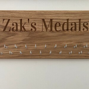May include: A wooden medal display with the text "Zak's Medals" engraved on the top. The display has 15 hooks for hanging medals.
