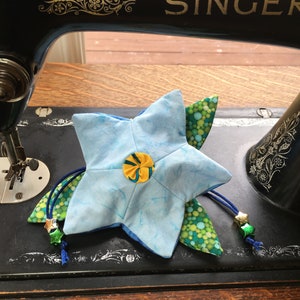 May include: A blue star-shaped fabric pouch with a yellow and green floral design. The pouch has a drawstring closure and is decorated with green and gold beads.