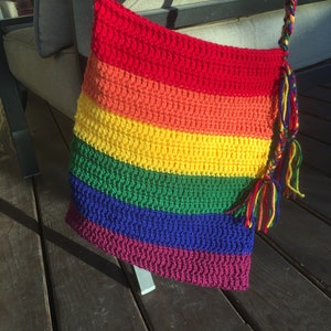 May include: A rainbow crocheted bag with a long strap. The bag is made of red, orange, yellow, green, blue, and purple yarn.