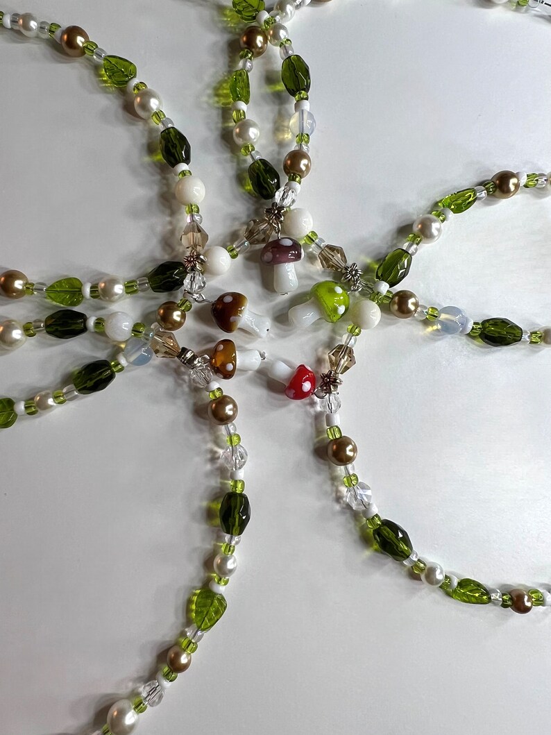 Pode incluir: Um colar de contas feito &agrave; m&atilde;o com um design caprichoso. O colar incorpora contas verdes, brancas e douradas, juntamente com pequenos pingentes de cogumelos. As contas s&atilde;o enfiadas para criar um acess&oacute;rio &uacute;nico e atraente.