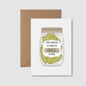 Peut inclure: Carte de vœux avec une illustration de bocal de cornichons. Le bocal a un couvercle en métal et une étiquette avec l'inscription "You mean a great dill to me". La carte est accompagnée d'une enveloppe marron.