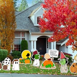 May include: A colorful Halloween yard decoration set featuring cartoon ghosts, pumpkins, and witches. The decorations are placed on a green lawn in front of a house with autumn foliage. A sign reads "Welcome Great Pumpkin."