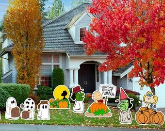 May include: A colorful Halloween yard decoration set featuring cartoon ghosts, pumpkins, and witches. The decorations are placed on a green lawn in front of a house with autumn foliage. A sign reads "Welcome Great Pumpkin."
