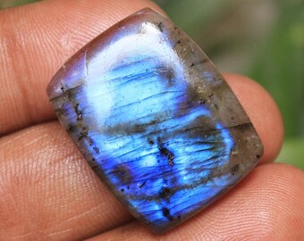 May include: A blue and gray labradorite gemstone cabochon with iridescent flashes of color. The gemstone is cut in a rectangular shape and has a smooth, polished surface.