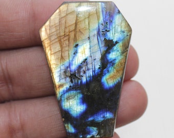 May include: A large, iridescent labradorite gemstone cabochon in a coffin shape. The stone has a mix of brown, blue, and green colors with a shimmering effect.