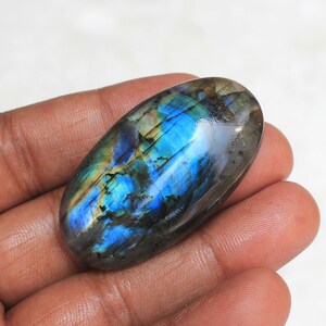 May include: A large, oval-shaped, iridescent labradorite gemstone with blue, green, and gold hues. The stone is smooth and polished.