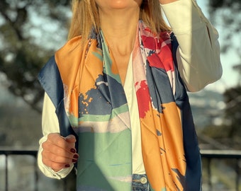 May include: A colourful silk scarf with abstract geometric patterns in shades of blue, green, orange, pink, and red. The scarf is draped around a person's neck and shoulders.