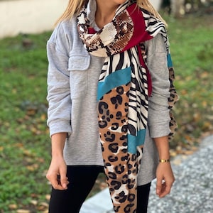May include: A long scarf with a variety of animal print patterns, including snake, zebra, and leopard. The scarf is a mix of brown, white, black, and teal.