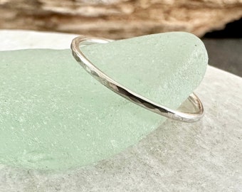 May include: A thin silver hammered band ring. The ring is sitting on a light green piece of sea glass.