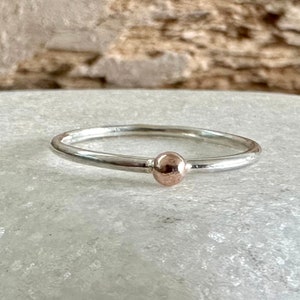 May include: A simple silver band ring with a single rose gold bead in the centre.