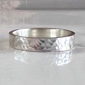 May include: A silver hammered band ring. The ring is wide and has a textured surface.