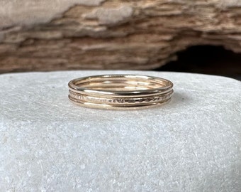 May include: Three gold stacking rings with a hammered texture. The rings are stacked on top of each other and are on a white background.