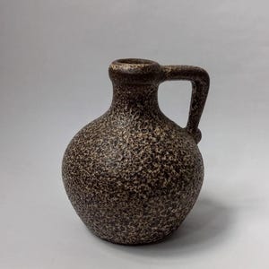 May include: A small, brown ceramic pitcher with a handle. The pitcher has a speckled texture and a rounded body. The handle is a simple loop shape. The pitcher is likely used for decorative purposes or for serving liquids.