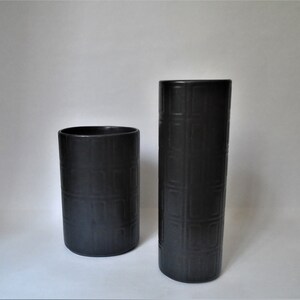 May include: Two black ceramic vases with a geometric pattern. The taller vase is on the right and the shorter vase is on the left.