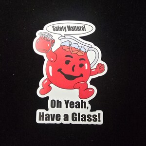 May include: A sticker featuring a cartoon red pitcher character with a smiling face, holding a glass of red liquid. The text "Safety Matters!" is above the character, and "Oh Yeah, Have a Glass!" is below.