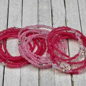 May include: A set of pink and clear beaded waist beads. The beads are arranged in a circular pattern and are made of glass. The beads are strung on a clear elastic cord.