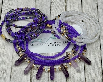 May include: A collection of beaded waist beads in shades of purple, white, and gold. Some strands feature amethyst crystal pendants. The image includes a card with the text "SELF LOVE & MANIFEST BOUTIQUE".