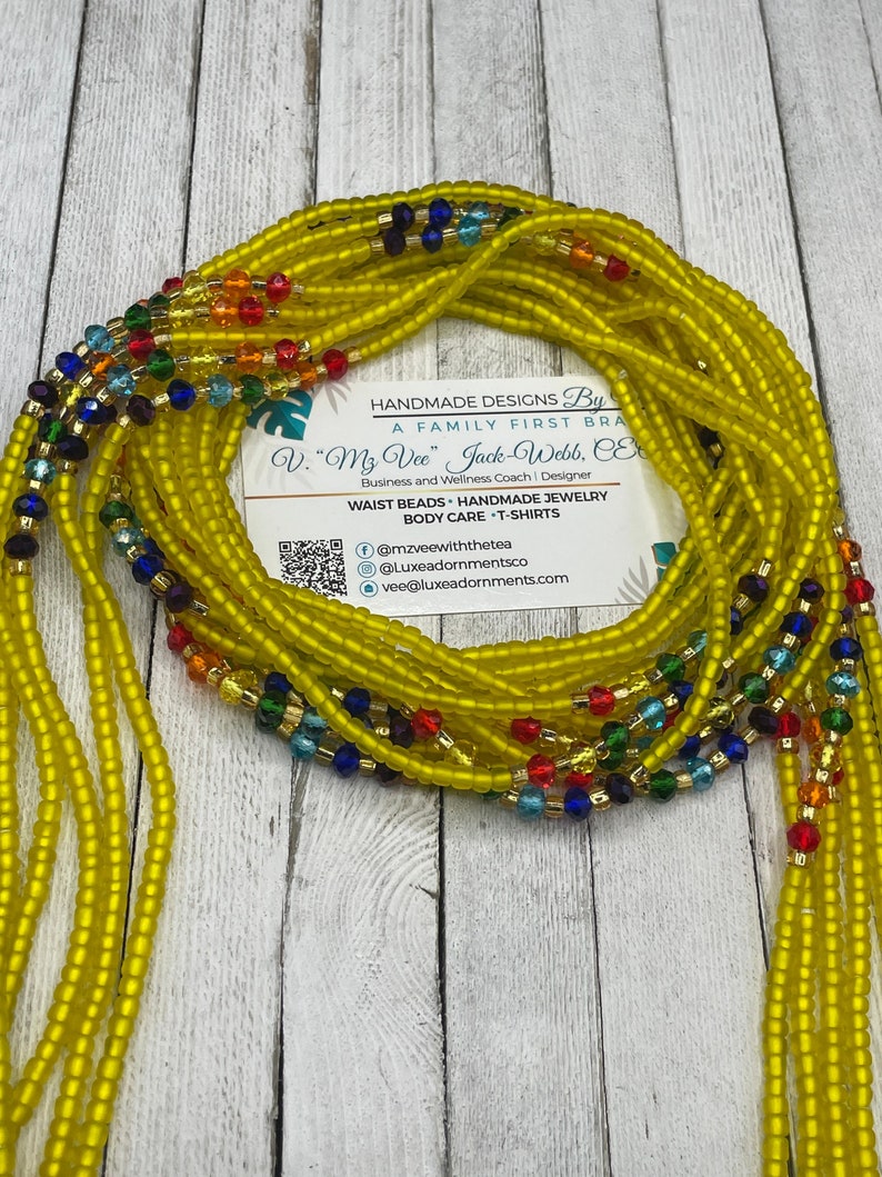 May include: A close-up of a yellow waist bead set with colorful beads. The beads are arranged in a circle and are made of glass. The beads are strung on a string and are tied together at the ends. The beads are a popular accessory for women and are often worn as a symbol of beauty and femininity.