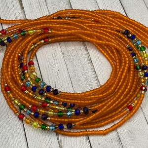 May include: Orange waist beads with strands of colorful beads. The beads are a mix of orange, red, yellow, green, blue, and gold. The beads are strung together to create a beautiful and unique accessory.