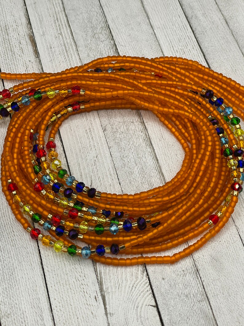May include: Orange waist beads with strands of colorful beads. The beads are a mix of orange, red, yellow, green, blue, and gold. The beads are strung together to create a beautiful and unique accessory.