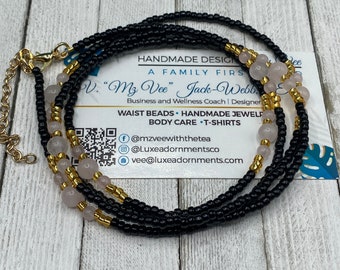May include: Black and gold waist beads with pink beads and a gold clasp. The beads are on a white surface with a business card that says "Handmade Designs, A Family First, PV. "My Vee" Jack-Webb, Business and Wellness Coach | Designer, Waist Beads - Handmade Jewelry, Body Care - T-Shirts, f@mzveewiththetea, @Luxeadornmentsco, vee@luxeadornments.com".