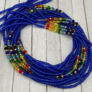 May include: A collection of blue waist beads with colorful accents. The beads are a deep blue, with sections of rainbow-colored beads and gold-colored spacers. The beads are arranged in a circular pattern, suggesting they are ready to wear.
