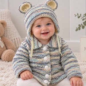 May include: A hand-crocheted baby cardigan and matching bonnet with bear ears, crafted from variegated yarn in shades of blue, cream, and grey. The cardigan features a collared neckline, long sleeves, and five white buttons down the front center.