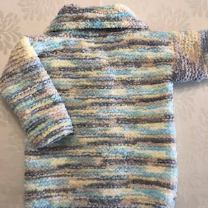 May include: A long-sleeved sweater crafted from fuzzy, textured yarn featuring a variegated color palette of soft yellow, light blue, white, and grey. The garment includes a wide, folded collar and a straight hemline, showcasing a consistent horizontal striped pattern throughout the entire piece.