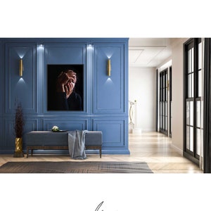 May include: A black and white photograph of a person with their hands covering their face, hanging on a blue wall in a modern interior design setting. The photograph is framed and hangs above a gray bench with a gray throw blanket.