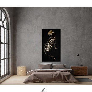 Op de afbeelding: Een zwarte en gouden cheeta-print kunstprint op een zwarte achtergrond. De cheetah kijkt naar links en zit. De print hangt aan een grijze muur in een kamer met een bed en een nachtkastje.