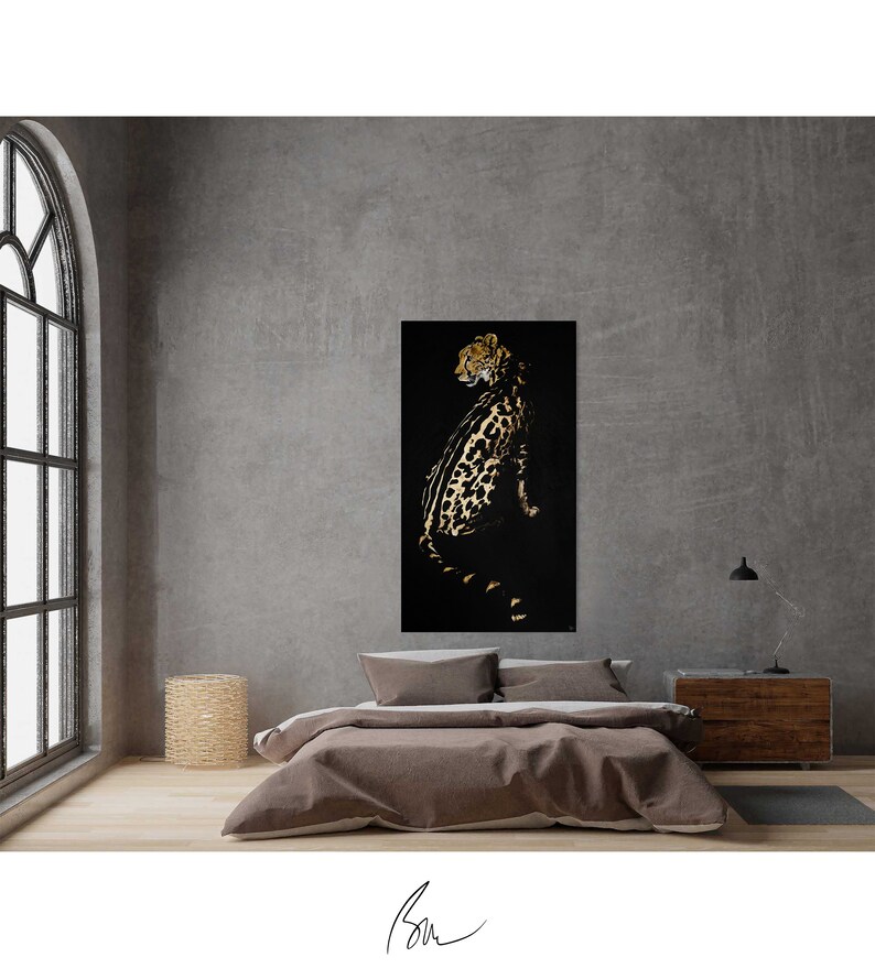 Op de afbeelding: Een zwarte en gouden cheeta-print kunstprint op een zwarte achtergrond. De cheetah kijkt naar links en zit. De print hangt aan een grijze muur in een kamer met een bed en een nachtkastje.