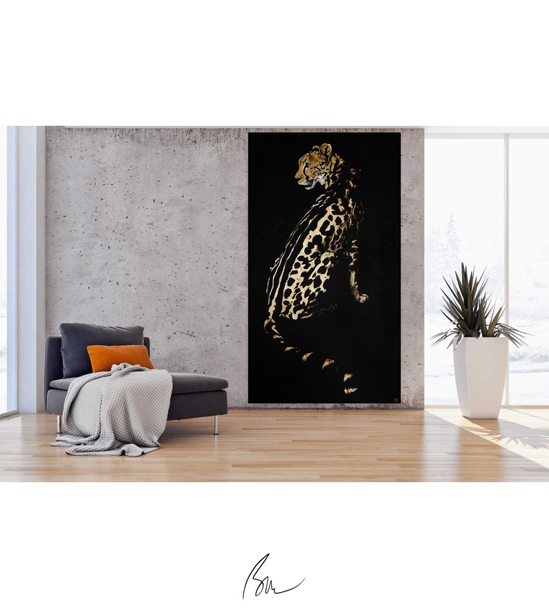 Op de afbeelding: Een zwart en gouden luipaardprint schilderij op een zwarte achtergrond. De luipaard zit en kijkt naar links. Het schilderij is ingelijst en hangt aan een muur in een kamer met een bank en een plant.