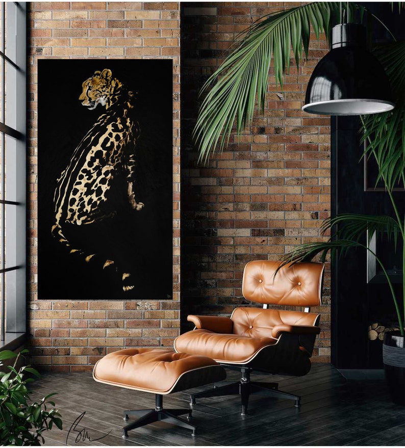 Op de afbeelding: Een zwart en gouden canvas wandkunstprint met luipaardprint, hangend aan een bakstenen muur boven een bruine leren fauteuil en voetenbank.