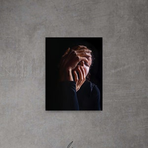 May include: A black and white photograph of a person with their hands covering their face. The person is wearing a black shirt and has dark hair.