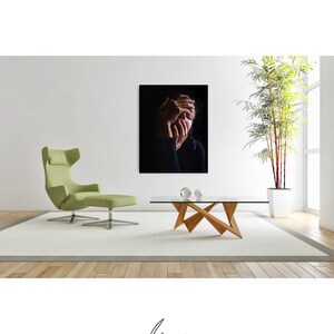 May include: A black and white photograph of a person with their hands covering their face. The photo is framed and hanging on a white wall above a wooden coffee table.