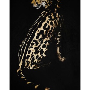 Op de afbeelding: Een zwart en gouden schilderij van een cheetah die op een zwarte achtergrond zit. De cheetah kijkt naar links en zijn vacht is gedetailleerd met zwarte vlekken en strepen.