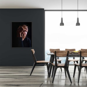May include: A black and white photo of a person with their hands covering their face, hanging on a black wall in a modern dining room with a wooden table and chairs.