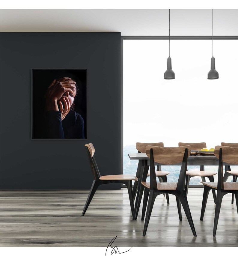 May include: A black and white photo of a person with their hands covering their face, hanging on a black wall in a modern dining room with a wooden table and chairs.