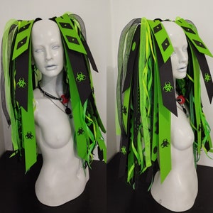 May include: Black and green hair extensions with biohazard symbols. The extensions are made of ribbon and are tied together with a black ribbon.