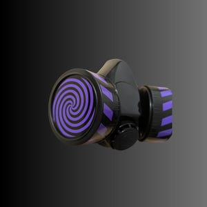 Pu&ograve; includere: Una maschera antigas nera con un design a spirale viola e nero sul davanti. La maschera ha un cinturino nero e un filtro nero.
