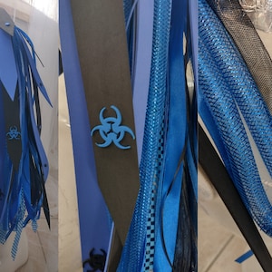 May include: Blue and black hair extensions with a biohazard symbol on a black leather strap. The extensions are made of a variety of materials, including ribbon, mesh, and fringe.