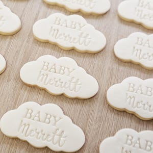 May include: A close-up of nine white cloud-shaped cookies with the text "BABY Merrett" embossed on each cookie.